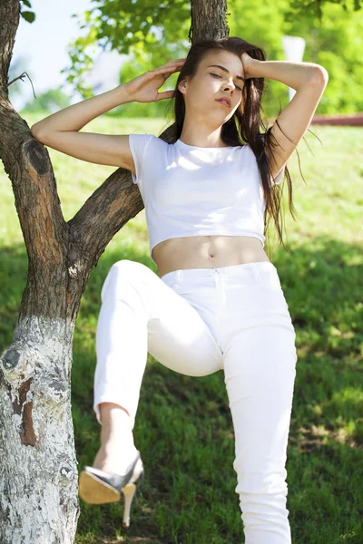 Hermosa mujer morena posando contra el parque de verano, sol brillante —  Fotos de Stock