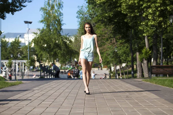 Joven mujer morena hermosa en una blusa azul y pantalones cortos walki —  Fotos de Stock