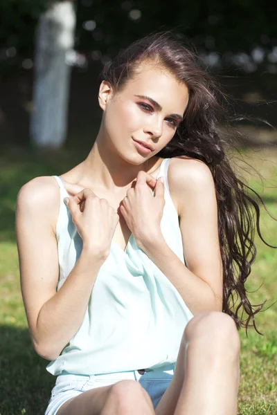 Young brunette woman in a turquoise blouse posing sitting on a g — Stock Photo, Image
