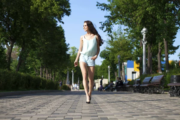 Joven mujer morena hermosa en una blusa azul y pantalones cortos walki —  Fotos de Stock