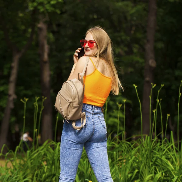 Молодая красивая женщина с сотовым телефоном гуляет в летнем парке — стоковое фото