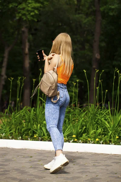 Young beautiful woman with a cell phone walks in the summer park — Stockfoto