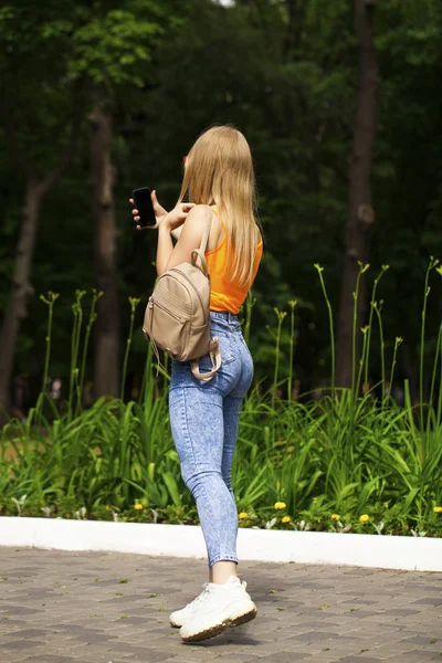 Joven hermosa mujer con un teléfono celular camina en el parque de verano —  Fotos de Stock