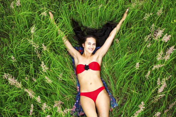 Çim üstünde yatan kırmızı mayo seksi esmer kadın — Stok fotoğraf