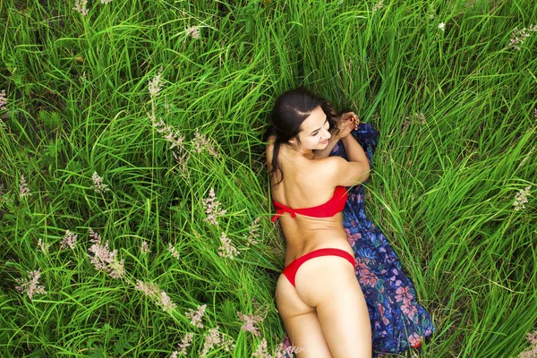 Sexy brunette woman in a red bathing suit lying on the grass top — Stock Photo, Image