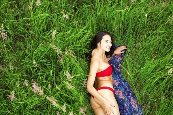 섹시한 갈색 머리 여자 에 a 빨간 수영복 누워 에 그만큼 잔디 상단 — 스톡 사진