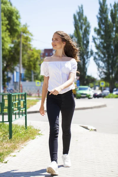 Jonge mooie brunette vrouw in jeans en witte blouse wandelen — Stockfoto