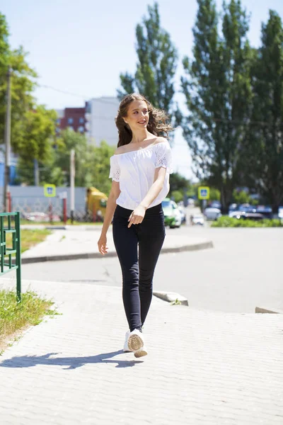 Jonge mooie brunette vrouw in jeans en witte blouse wandelen — Stockfoto