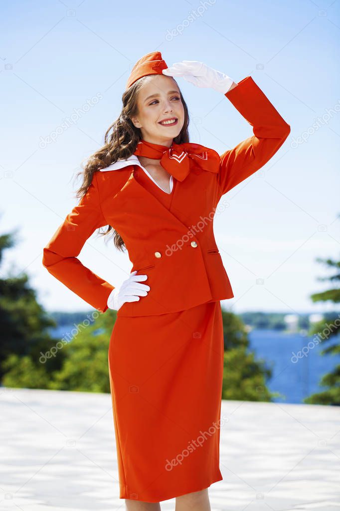 Beautiful stewardess dressed in official red uniform gainst a bl