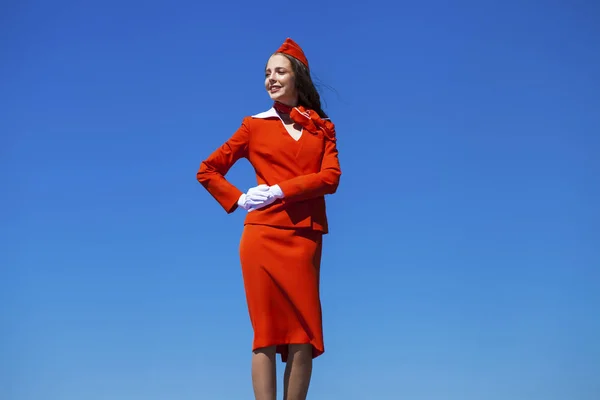 Vackra flygvärdinna klädd i officiella Red Uniform gainst en bl — Stockfoto
