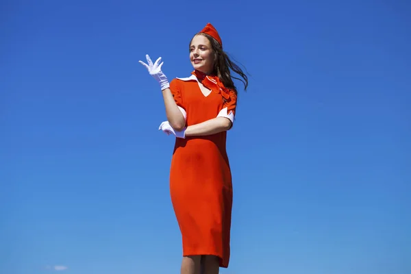 Vackra flygvärdinna klädd i officiella Red Uniform gainst en bl — Stockfoto