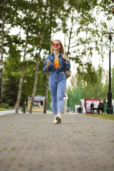 Ung blond kvinna i blå jeans går i sommarpark — Stockfoto
