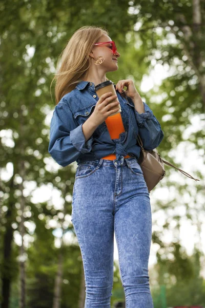 Gadis pirang dengan celana jeans biru berjalan di taman musim panas — Stok Foto