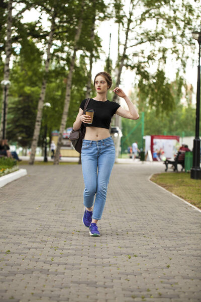 Young beautiful brunette girl in jeans and t-shirt walking in su