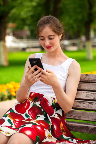 Telefonisch. schönes Mädchen im Sommerkleid sitzt auf einem pa — Stockfoto