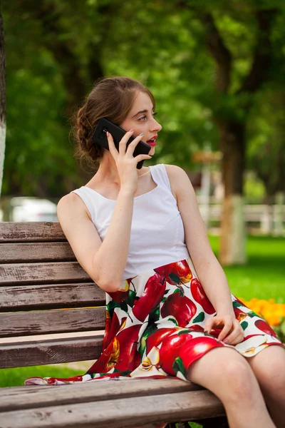 Telefonisch. schönes Mädchen im Sommerkleid sitzt auf einem pa — Stockfoto