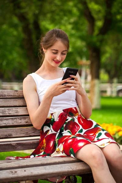 Telefonisch. schönes Mädchen im Sommerkleid sitzt auf einem pa — Stockfoto