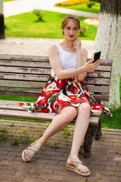 Llamando por teléfono. Hermosa chica en vestido de verano sentado en un pa — Foto de Stock