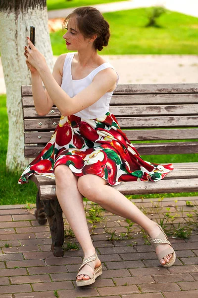 Τηλεφωνώ τηλεφωνικά. Όμορφο κορίτσι στο καλοκαίρι φόρεμα κάθεται σε ένα PA — Φωτογραφία Αρχείου