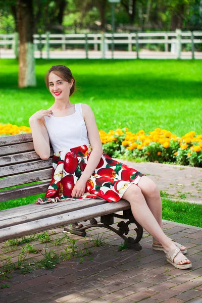 Menina bonita no vestido de verão sentado em um banco de parque — Fotografia de Stock