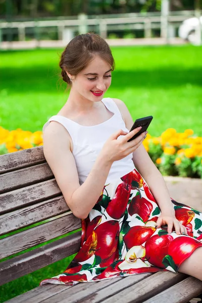 Ringer via telefon. Vacker flicka i sommarklänning sitter på en PA — Stockfoto