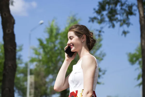 Portrait de jeune femme brune heureuse en robe parlant au téléphone, en plein air rue d'été — Photo