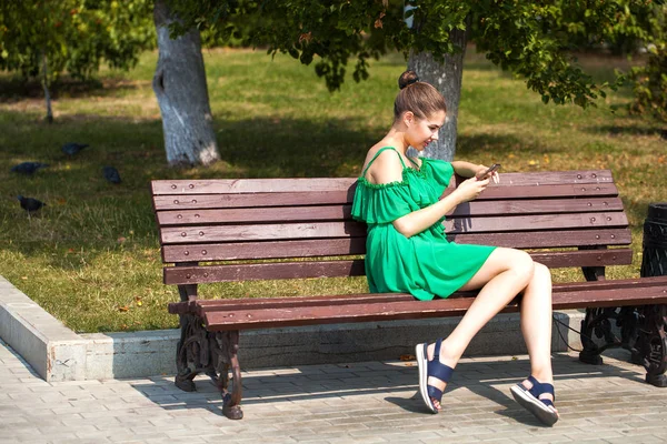 Sexy menina branca bonita em vestido verde sentado em um banco — Fotografia de Stock