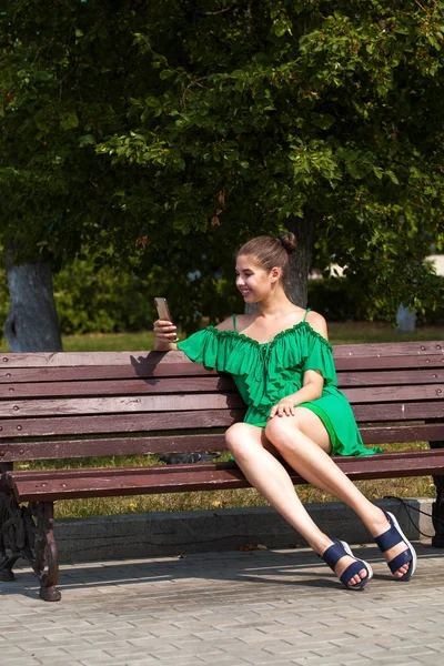 Sexig vacker kaukasiska flicka i grön klänning sitter på en bänk — Stockfoto