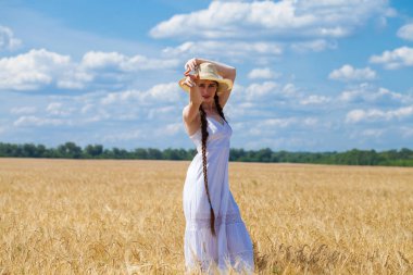 Beyaz elbiseli genç esmer kadın bir buğday tarlasında yürüyor