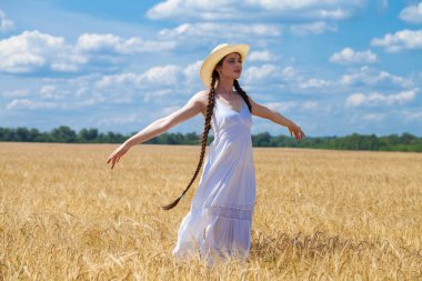 Beyaz elbiseli genç esmer kadın bir buğday tarlasında yürüyor