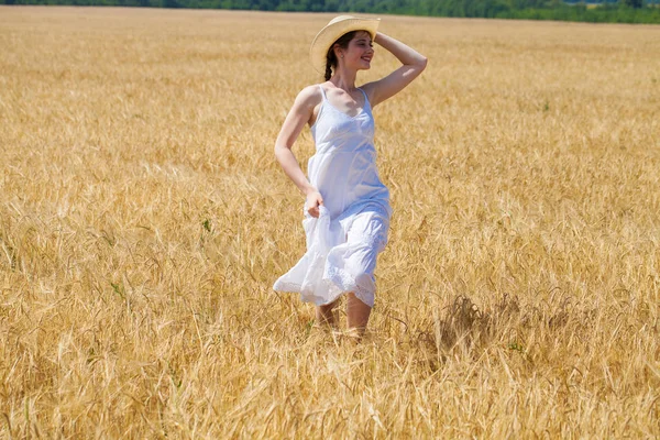 Young brunette woman in white dress walking in a wheat field — Stock Photo, Image