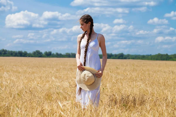 Beyaz elbiseli genç esmer kadın bir buğday tarlasında yürüyor