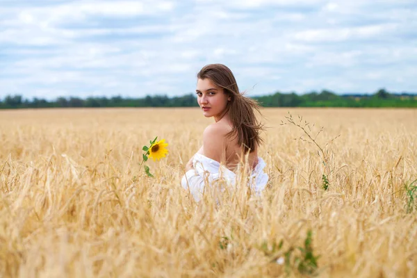 Menina loira jovem em vestido branco andando em um campo de trigo — Fotografia de Stock