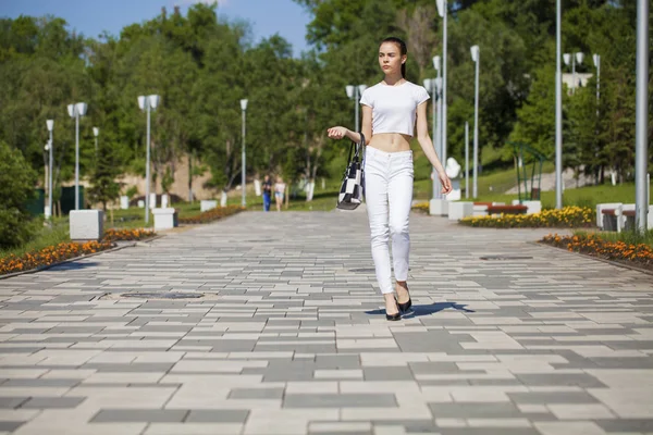 Joven hermosa chica morena en jeans blancos y camiseta caminando —  Fotos de Stock