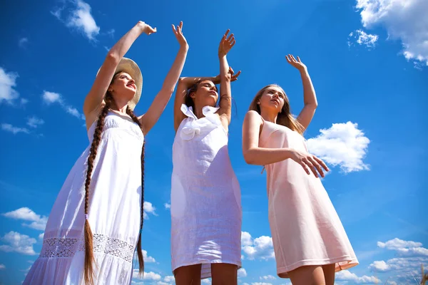 Drie jonge vrouwen in witte jurk poseren tegen de blauwe hemel in — Stockfoto