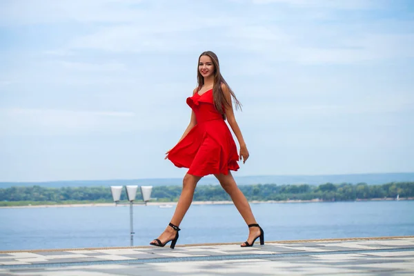 Ung, vakker modell i rød kjole som går på sommergaten – stockfoto