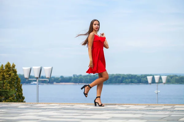 Young beautiful model in red dress walking on the summer street — Stock Photo, Image