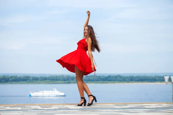 Young beautiful model in red dress walking on the summer street — Stock Photo, Image