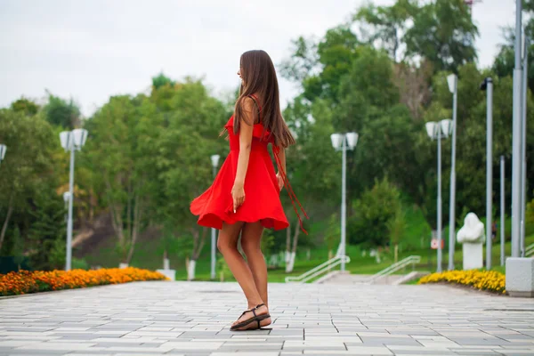 Молодая красивая женщина в красном платье ходит по летней улице — стоковое фото