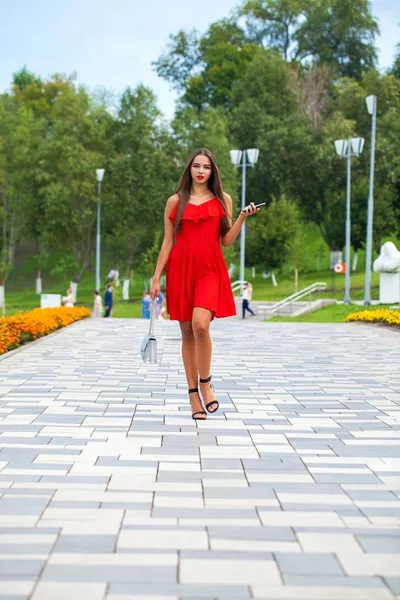 Νεαρό όμορφο μοντέλο με κόκκινο φόρεμα περπάτημα στο δρόμο του καλοκαιριού — Φωτογραφία Αρχείου