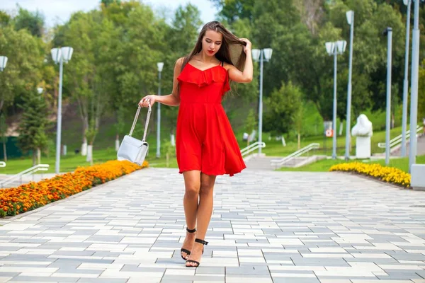 Young beautiful model in red dress walking on the summer street — Stock Photo, Image