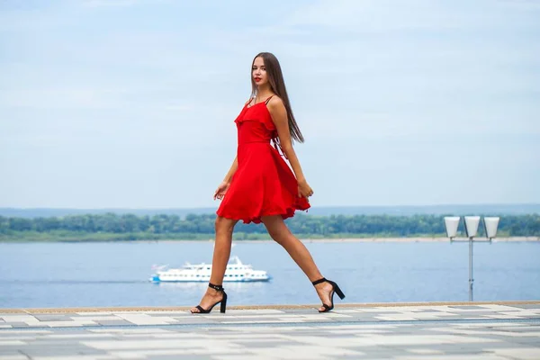 Young beautiful model in red dress walking on the summer street — Stock Photo, Image