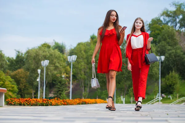 Kırmızı giysiler içinde iki şık güzel kız boyunca yürümek — Stok fotoğraf