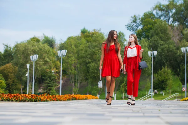 Dvě stylové krásné přítelkyně v červených šatech chodí po — Stock fotografie