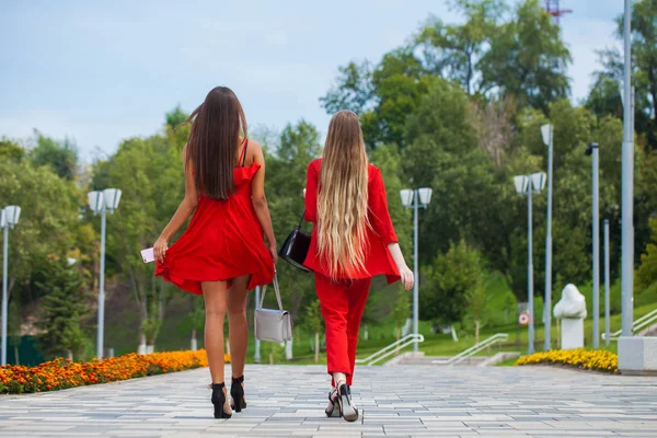 Two stylish beautiful girlfriends in red clothes walk along the — Stock Photo, Image