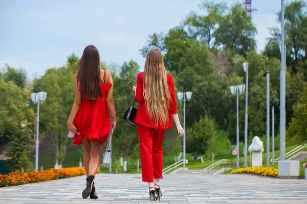 Duas belas namoradas elegantes em roupas vermelhas caminham ao longo do — Fotografia de Stock