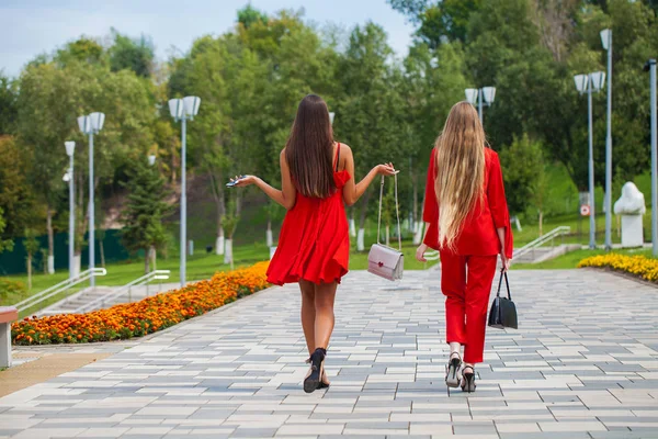 Two stylish beautiful girlfriends in red clothes walk along the — Stock Photo, Image