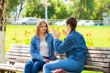 İki güzel kız arkadaş bir parkta bir ben üzerinde oturan konuşuyor