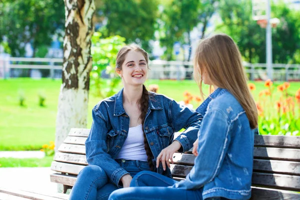 Två vackra flickvänner pratar i en Park sitter på en ben — Stockfoto