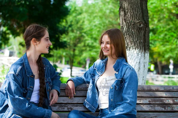 Två vackra flickvänner pratar i en Park sitter på en ben — Stockfoto